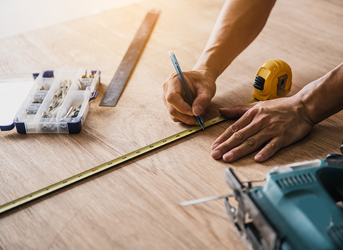 person measuring wood with tape measure and marking with pencil surrounded by tools for accurate woodworking projects with eight tools on the table